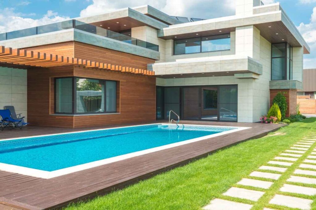 Modern two-storey home with a sleek custom lap pool, timber deck surrounds, and manicured lawn with stepping stones, featuring clean architectural lines and floor-to-ceiling windows.