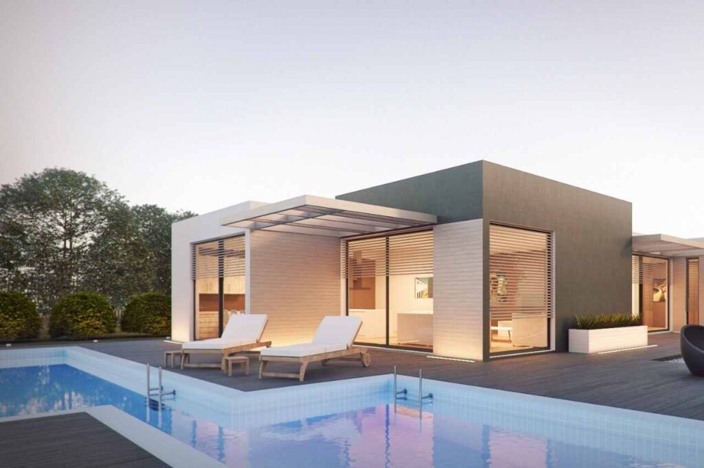 Modern single-storey villa with clean cubic architecture, featuring a geometric swimming pool, timber decking, sun loungers, and large glass windows with horizontal blinds, set against a serene outdoor backdrop.