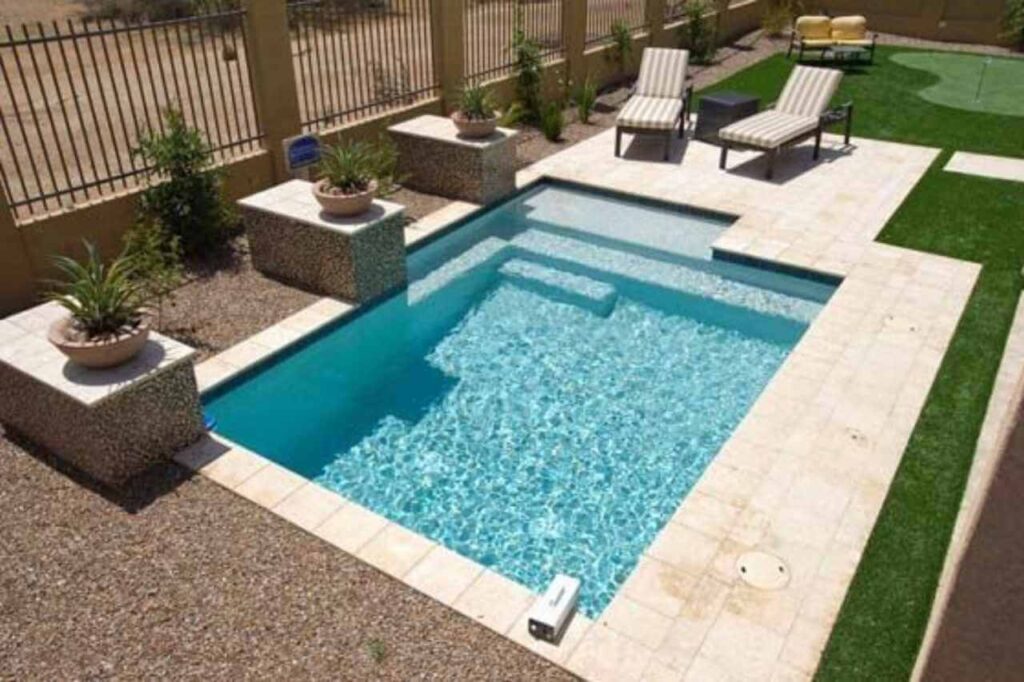 Compact inground plunge pool with light blue water and built-in entry steps, surrounded by beige stone pavers, lounge chairs, and desert landscaping in a small Newcastle backyard