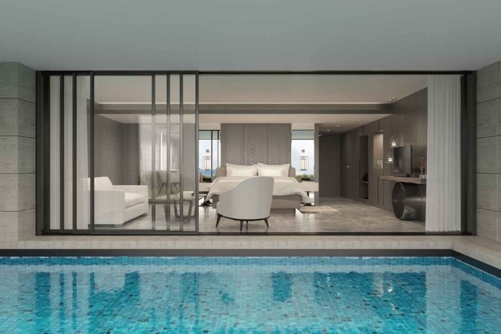 Luxury modern bedroom suite with floor-to-ceiling sliding glass doors opening directly onto a private indoor swimming pool with blue mosaic tiles, blending elegance and resort-style living.