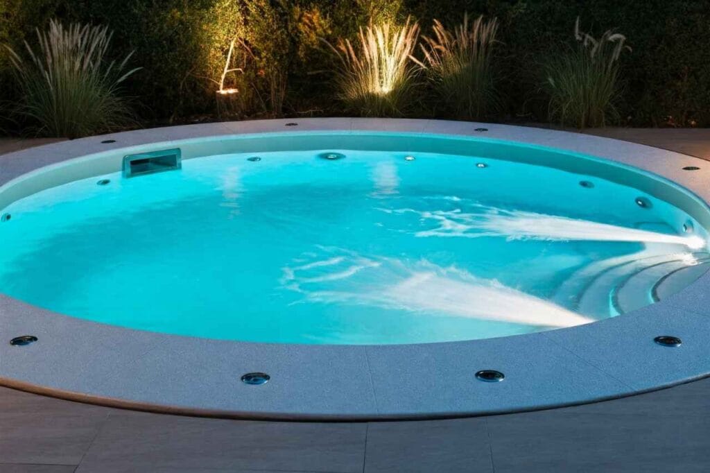 Round custom precast plunge pool with powerful spa jets and soft blue lighting, surrounded by modern tiling and lush garden landscaping, ideal for hydrotherapy and relaxation.
