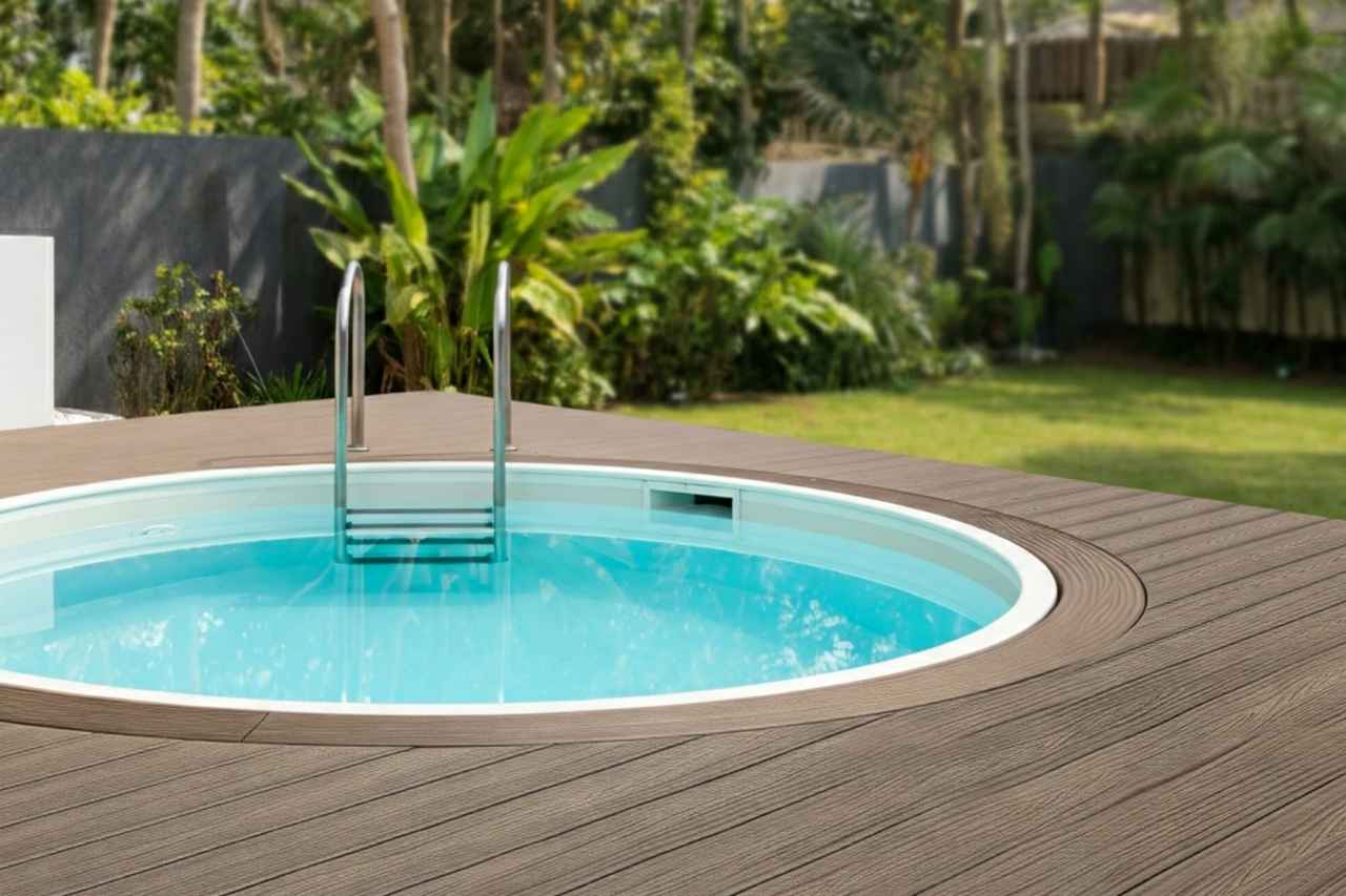 Circular precast plunge pool with timber-look decking and stainless steel ladder, set in a tropical-style Newcastle backyard with lush greenery and a private fence line.