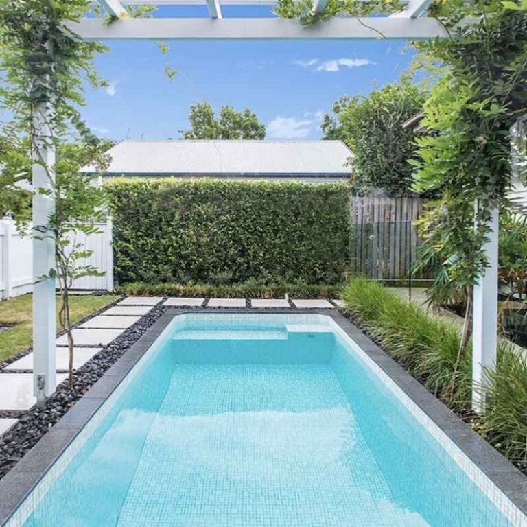 Rectangular inground plunge pool with tiled finish in a landscaped backyard with pergola, stepping stones, and greenery in Newcastle NSW