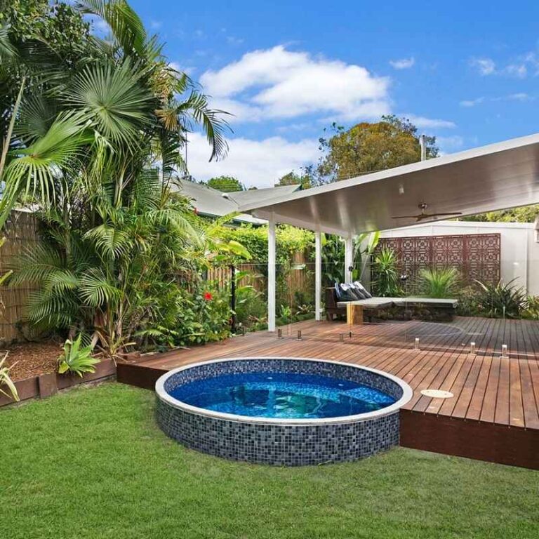 Round semi above ground plunge pool with dark mosaic tiles beside a timber deck and tropical landscaped backyard with pergola in Newcastle NSW
