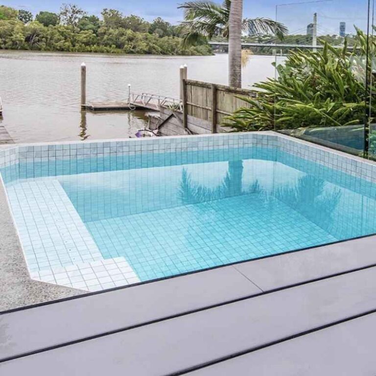 Modern square plunge pool with tiled interior overlooking a riverside backyard with private jetty and lush greenery in Newcastle NSW