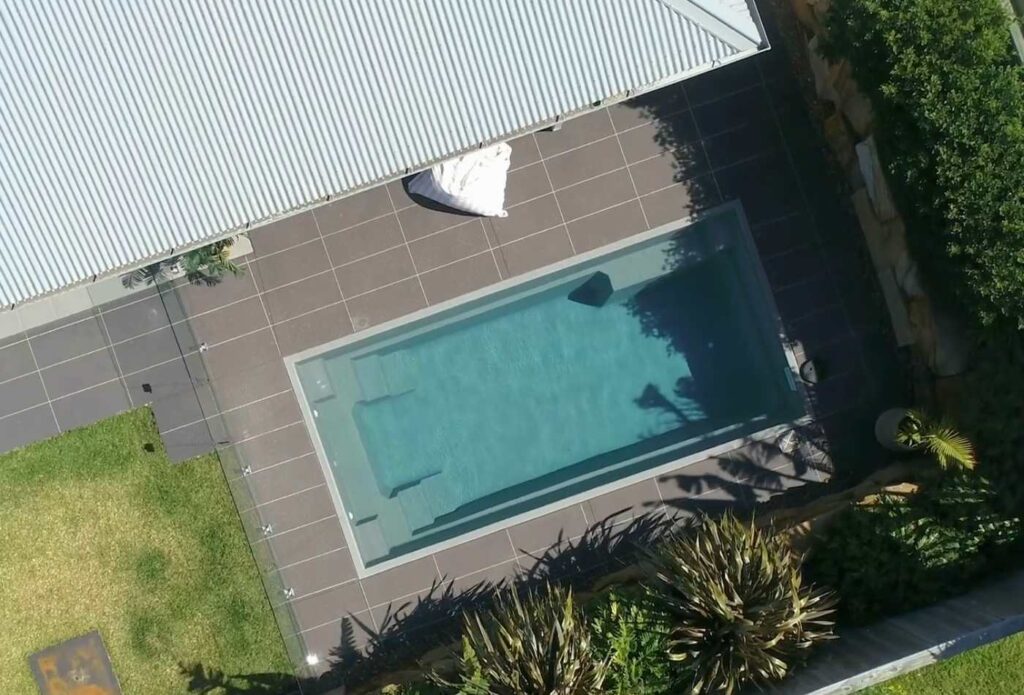 Aerial view of a rectangular fibreglass plunge pool with glass fencing and minimalist backyard landscaping in Gosford