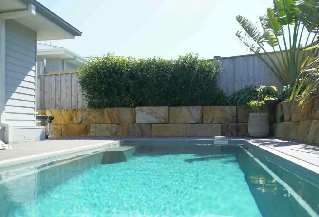 Ground-level view of a compact fibreglass swimming pool with landscaped retaining walls and modern backyard design in Gosford