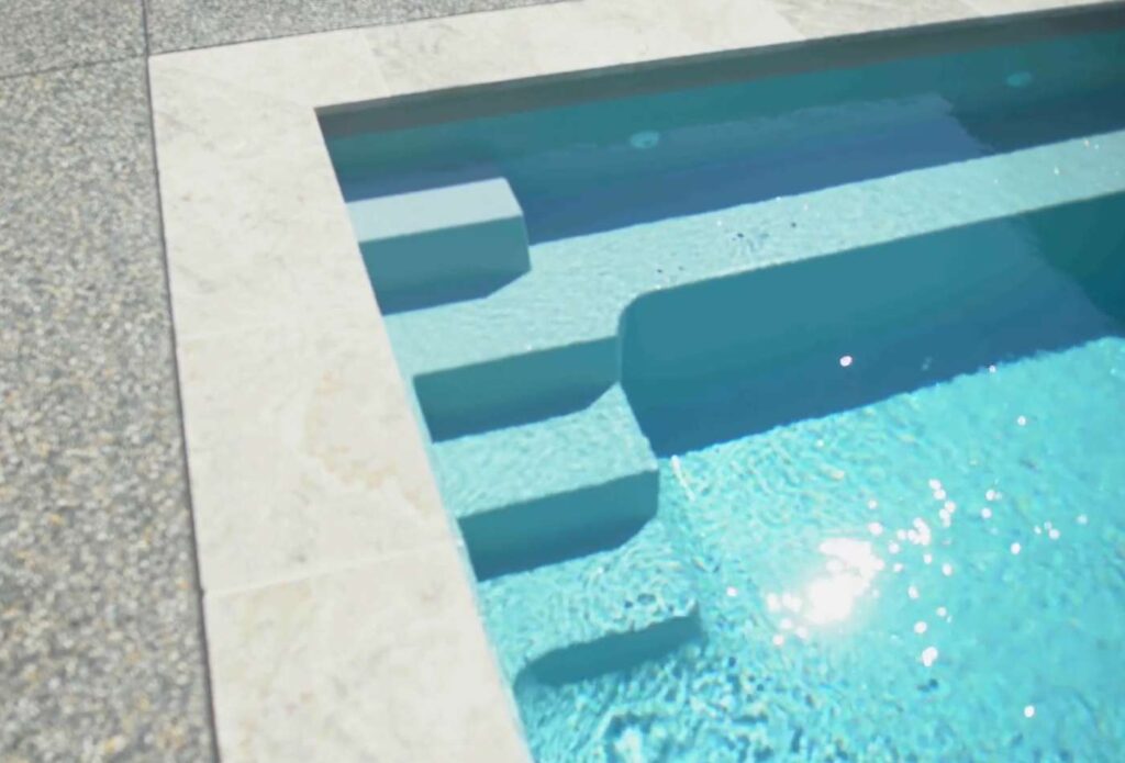 Close-up of fibreglass pool entry steps and tanning ledge with light stone coping in a modern Maitland backyard
