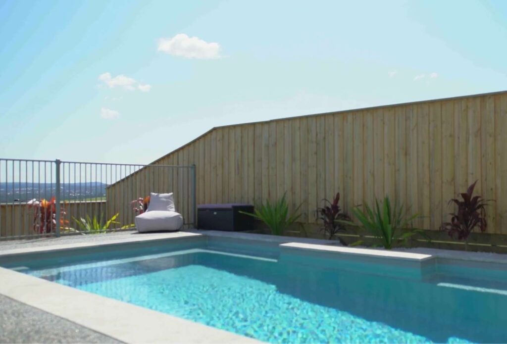 Side angle of a rectangular fibreglass swimming pool with elevated district views and exposed aggregate surrounds