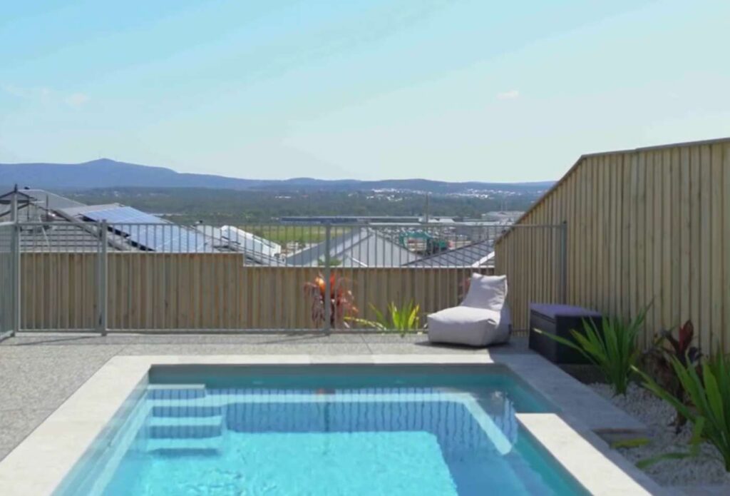 Front view of a modern fibreglass pool featuring built-in bench seating and minimalist backyard landscaping