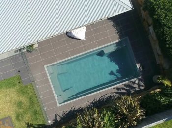 Aerial view of a rectangular fibreglass plunge pool with glass fencing and minimalist backyard landscaping in Gosford