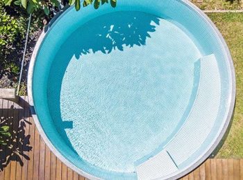 Aerial view of a circular plunge pool with light blue tiles surrounded by timber decking and greenery in Newcastle NSW