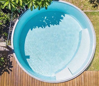 Aerial view of a circular plunge pool with light blue tiles surrounded by timber decking and greenery in Newcastle NSW