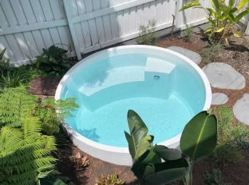 Round above ground plunge pool with light blue tiled interior surrounded by tropical plants and white fence in a compact backyard in Newcastle NSW
